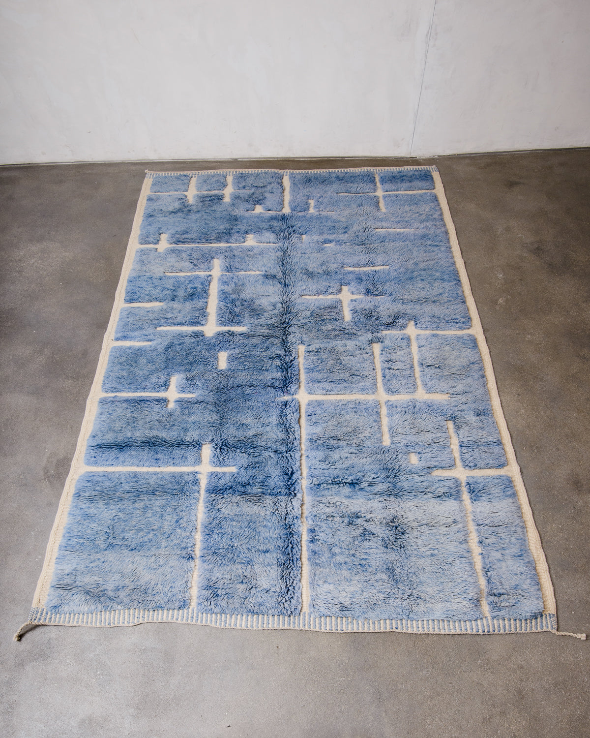 Berberlin Beni M'rirt Rug made of heavy wool pile in speckled denim blue and cream laying flat on concrete floor.